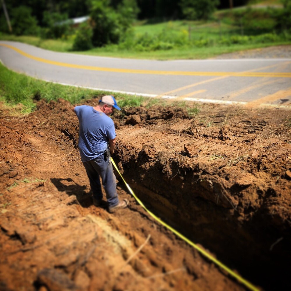 Sam measuring for drainage pipe down near paved road